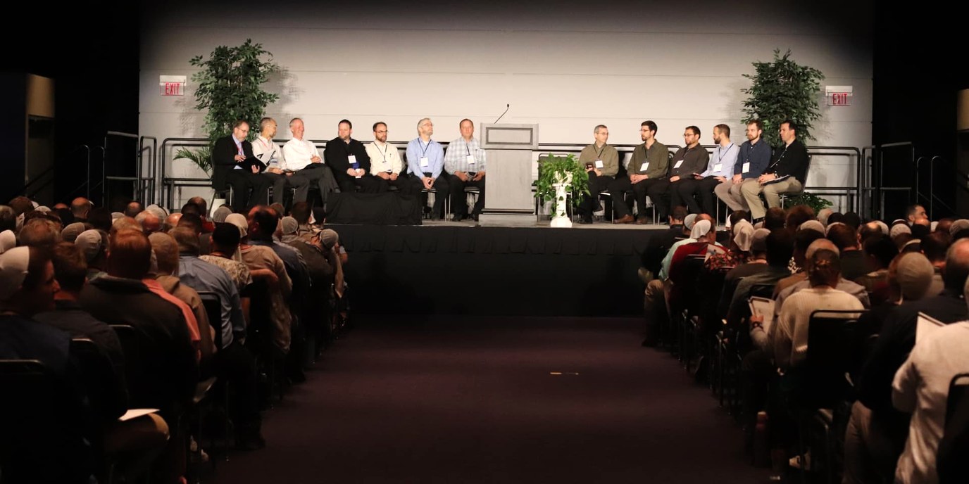 Speakers seated on the convention center stage with the audience in view